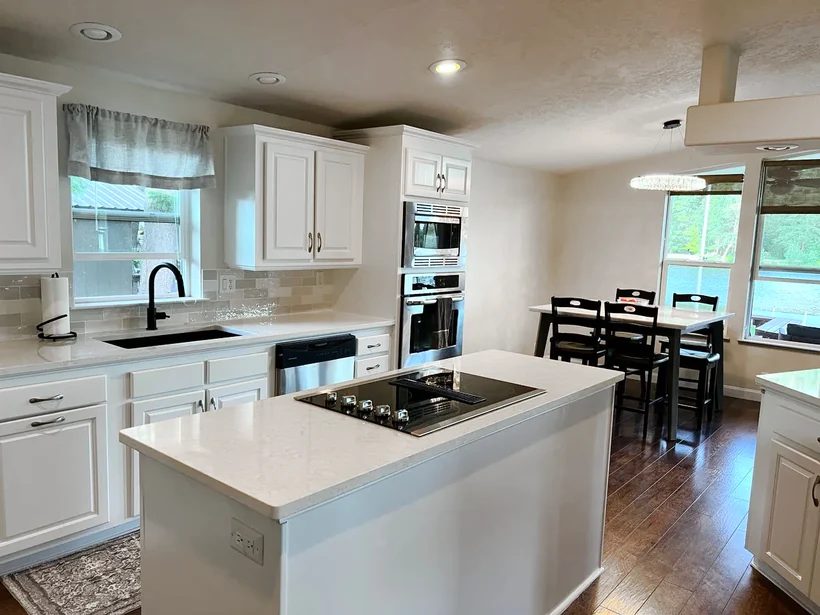 The same kitchen after remodeling, with white cabinets, quartz counters and hardwood floors