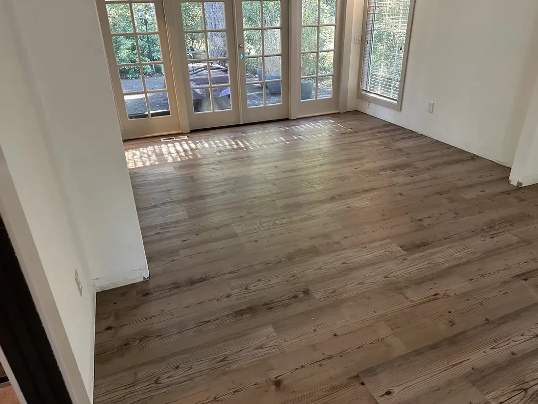 Wood-look plank flooring installed through an empty living room with French doors