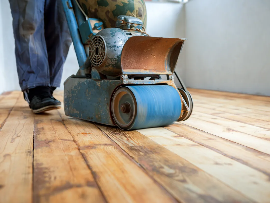 Drum sander taking a worn hardwood floor down to bare wood