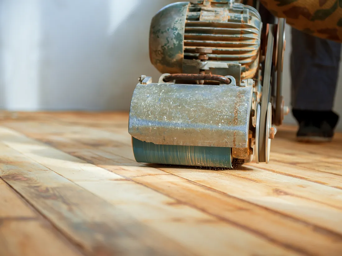 Close-up of a drum sander stripping the old finish off wood floorboards