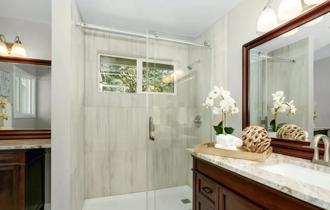Remodeled bathroom with a tiled walk-in shower, glass door and stone vanity top