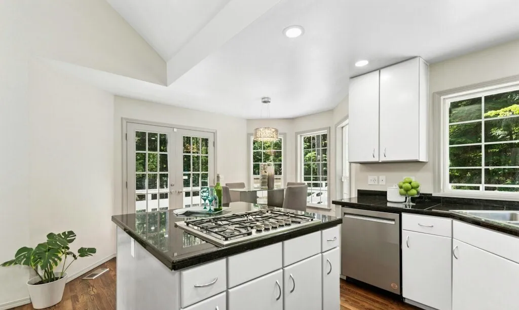 White kitchen with a stone-topped island, stainless dishwasher and vaulted ceiling